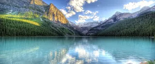 Auf dem Foto eine Landschaft mit See, Wiese und grünen Bäumen zu sehen