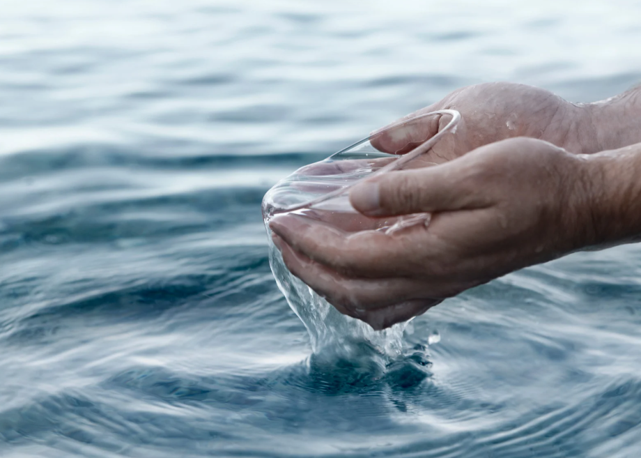 Es sind zwei Hände mit Wasser über dem Meer zu sehen